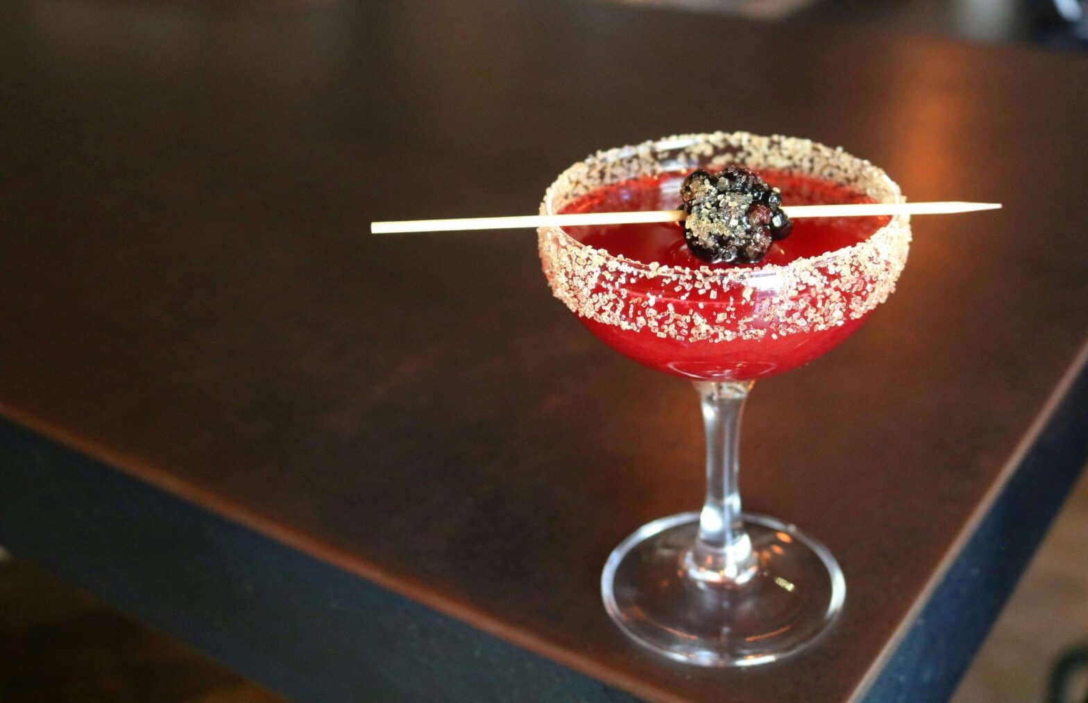 a red cocktail with a olive on a cocktail stick